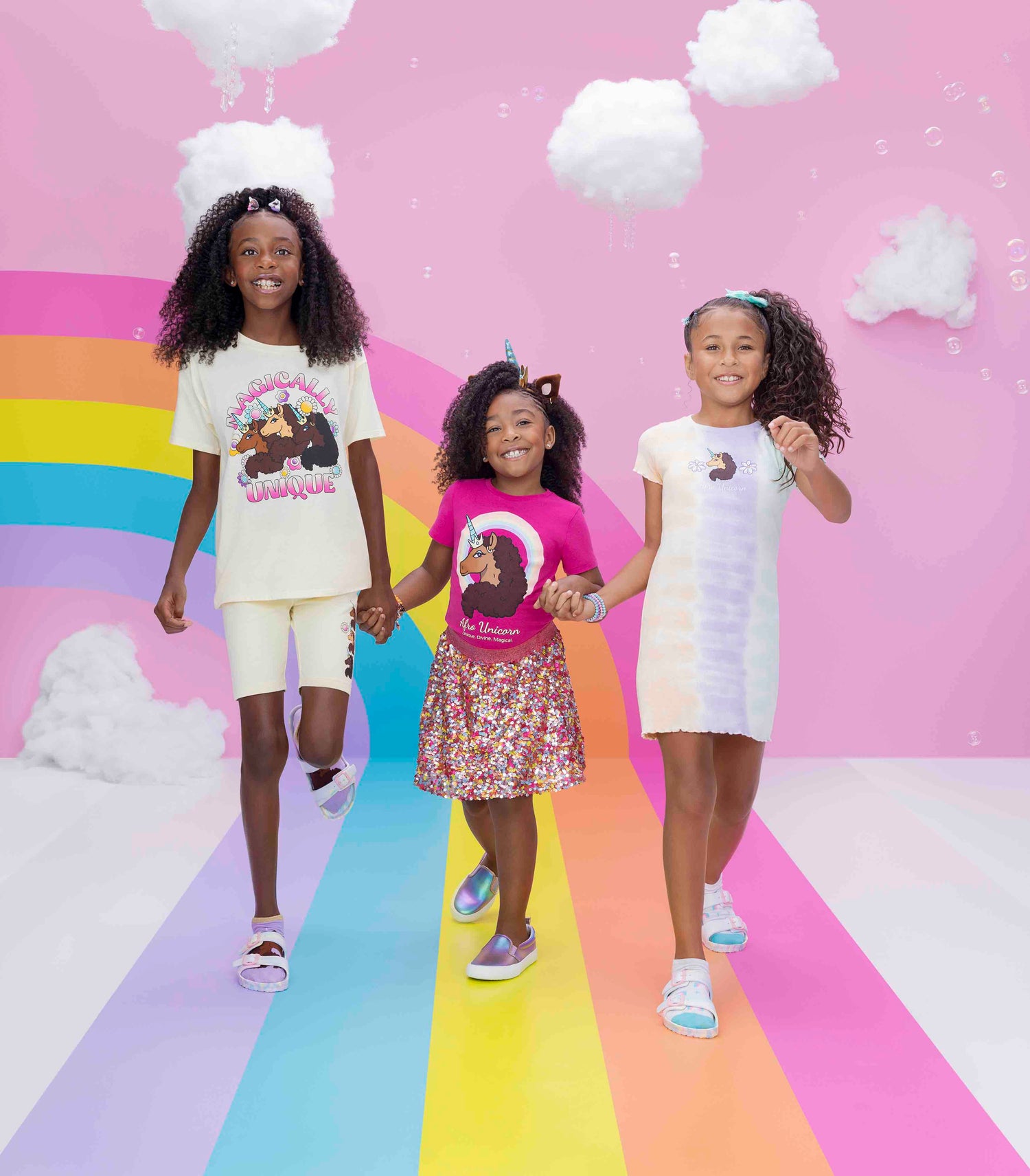 Three Afro Unicorn models holding hands in front of a rainbow walkway.