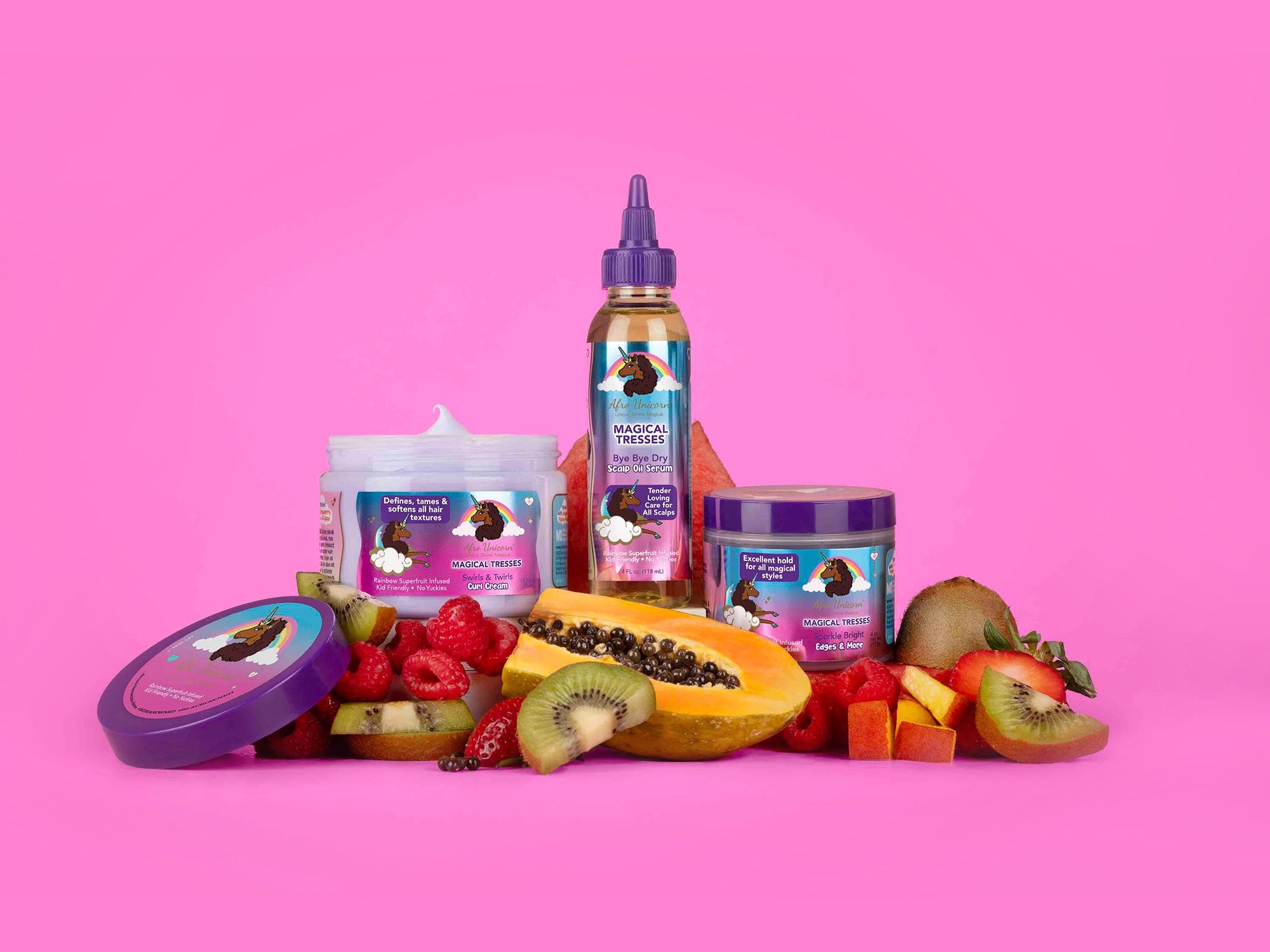 Afro Unicorn products with freshly cut fruit on a pink background.