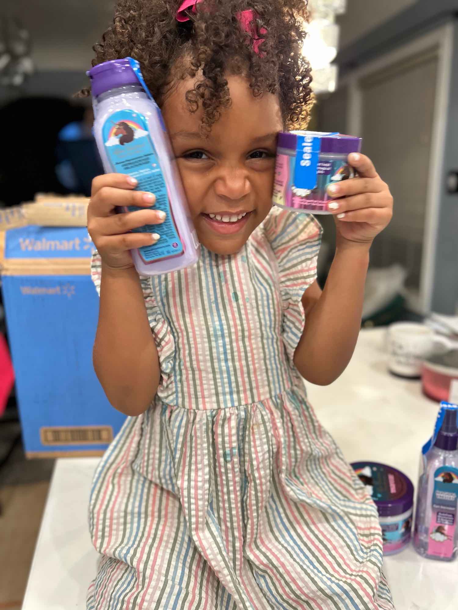 A child smiling while holding Afro Unicorn products.