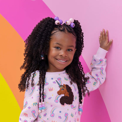 Afro Unicorn model with her hand on a rainbow painted wall.